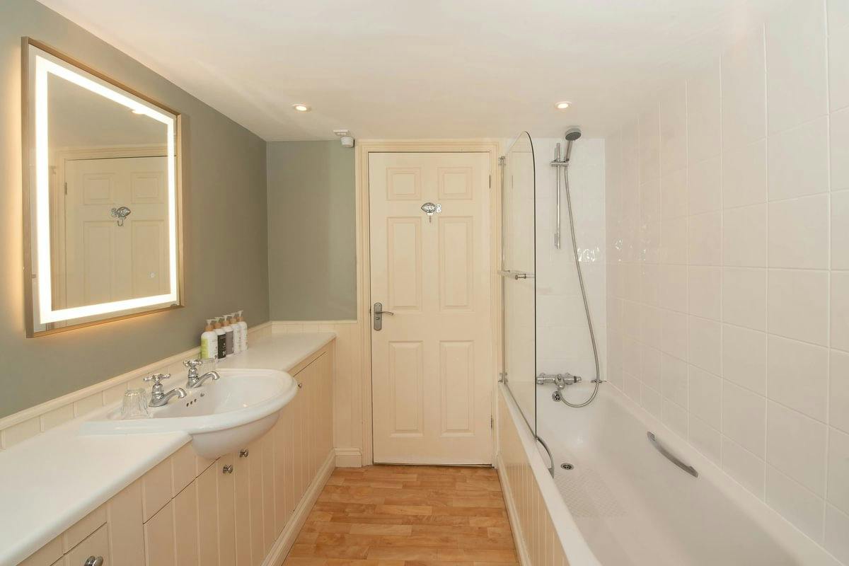 Modern bathroom with a lit mirror, sink, and bathtub with shower. Beige door and wood floor.
