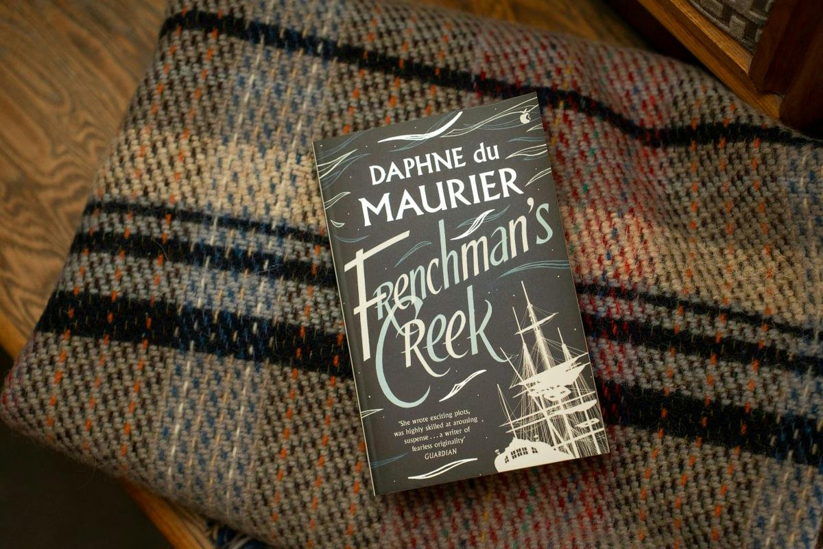 Book 'Frenchman's Creek' by Daphne du Maurier on a plaid blanket, featuring a ship illustration on the cover.