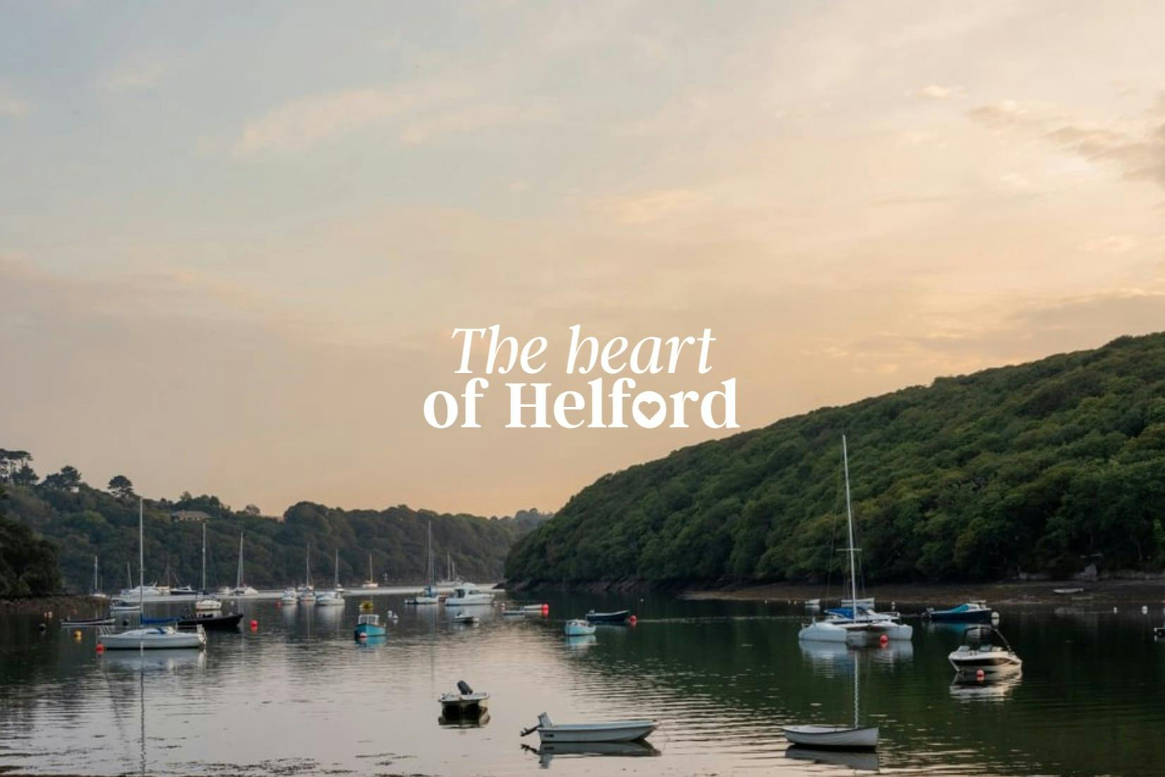 Boats on a calm river at sunset, surrounded by lush green hills. Text reads "The heart of Helford."