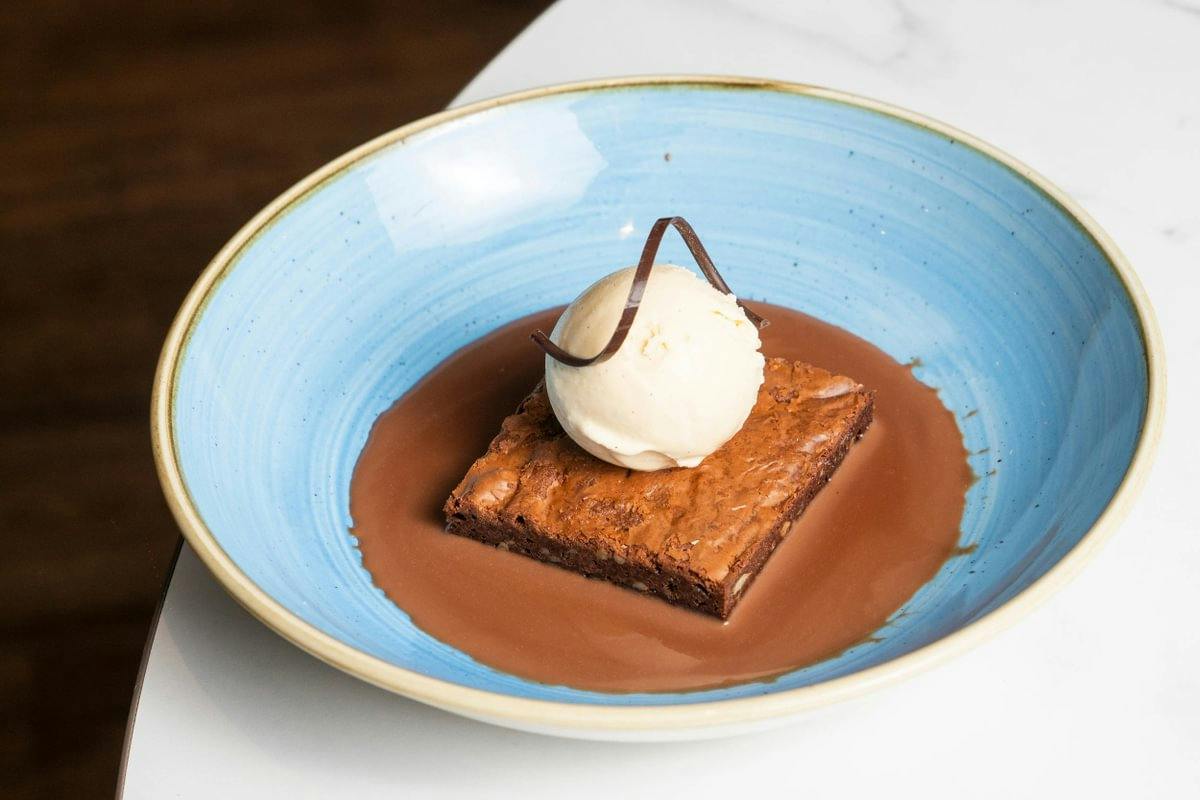 Brownie with vanilla ice cream and chocolate sauce in a blue bowl.