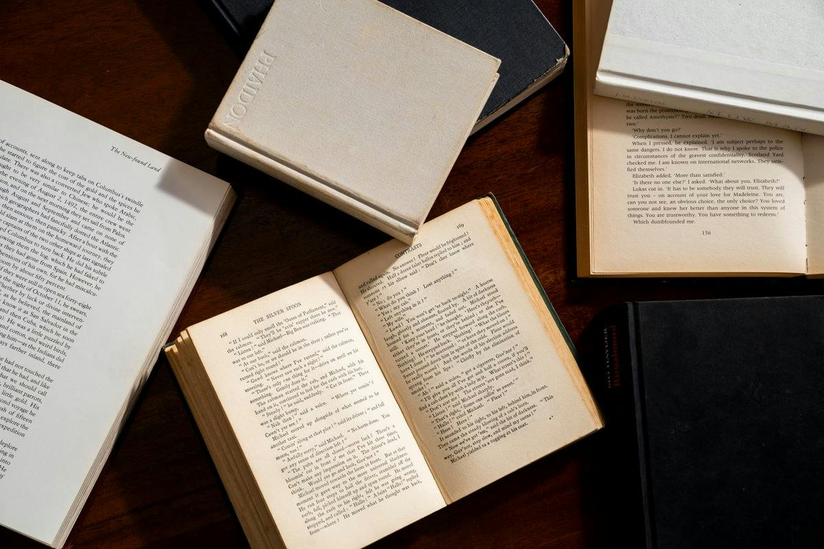 Several open and closed books arranged on a dark wooden table, including a small open vintage book at the centre.